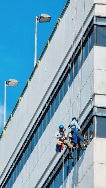Two workers cleaning windows on a glass building facade using a lift platform, enhancing building aesthetics.